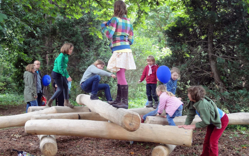 Kinder klettern und spielen auf Spilezeug-Skulptur aus Holzstämmen